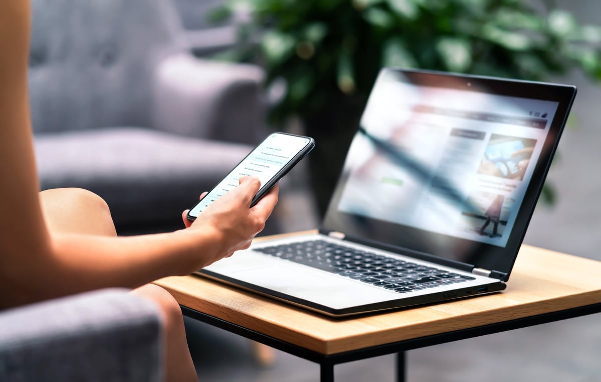 Woman using smartphone and laptop at café table — a simple website can support sales before, during and after opening hours