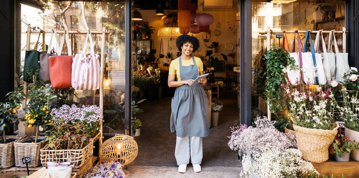 Florist owner smiling and using digital tablet in front of her flower shop, small business and entrepreneurship concept