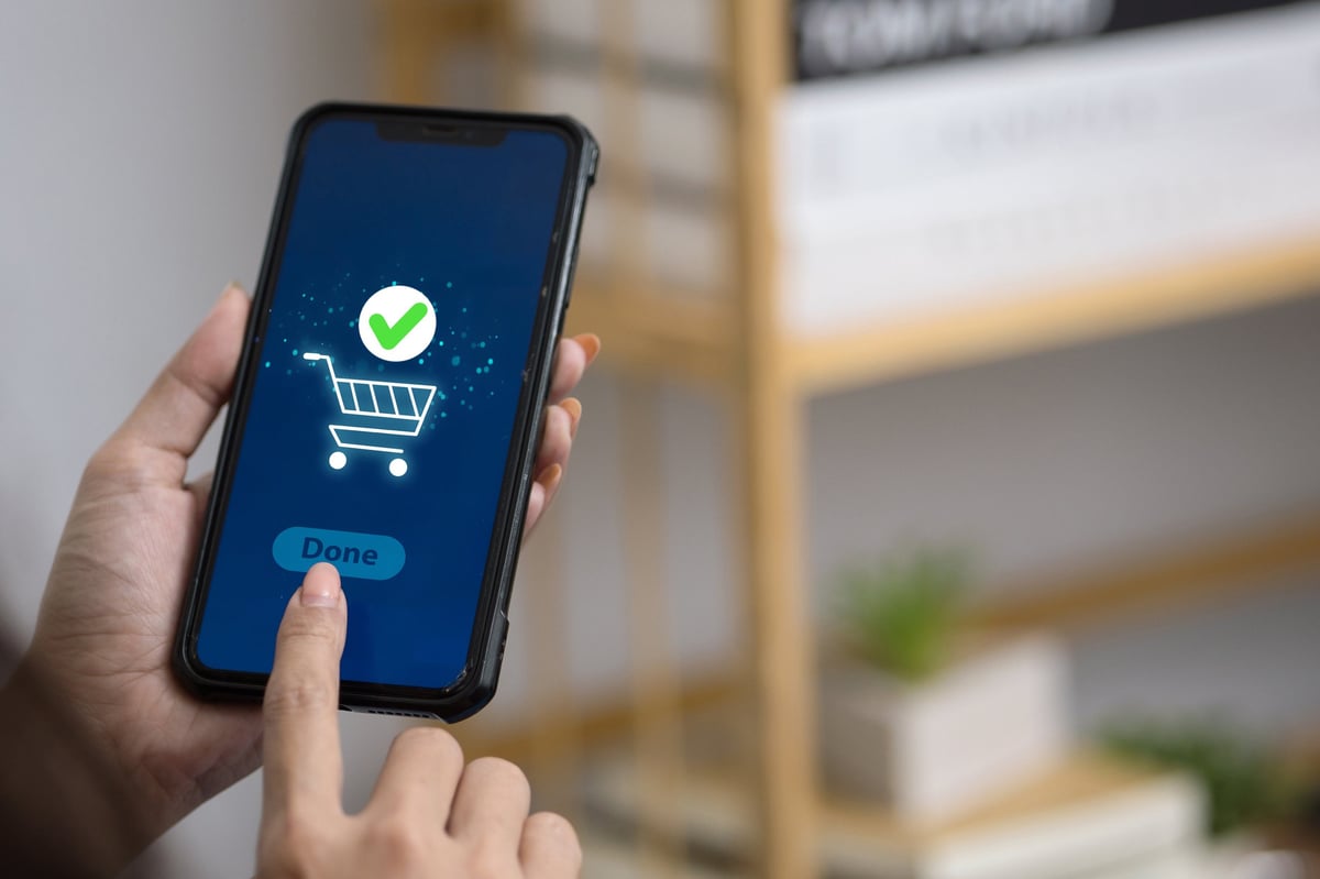 Woman confirming online shopping order via smartphone app with shopping cart and green check mark icon on screen