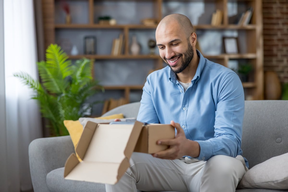 Cheerful customer unboxing a delivery package at home — details after the sale shape what people remember