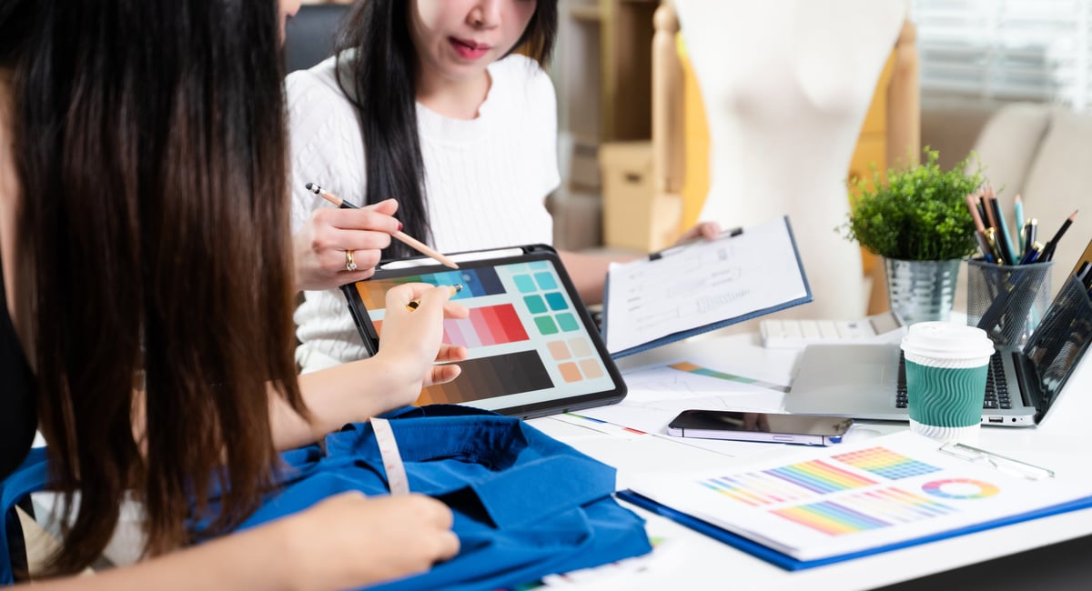 Designers working together with fabric and color palette on digital tablet — creative branding and identity design